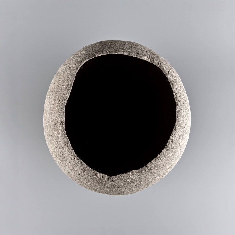 Pode incluir: Um vaso redondo de cer&acirc;mica cinza com uma superf&iacute;cie &aacute;spera e texturizada e uma grande abertura circular.