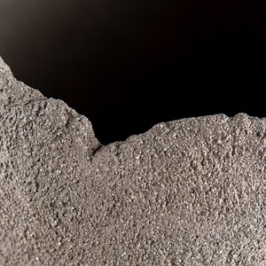 Pode incluir: Close-up de uma superf&iacute;cie &aacute;spera, cinza e texturizada com uma borda irregular.