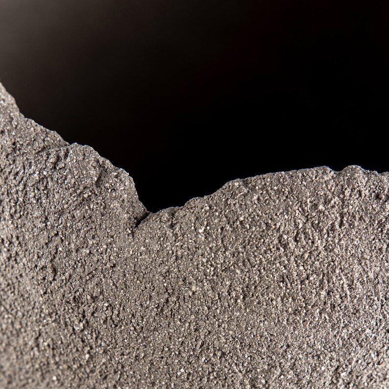 Pode incluir: Close-up de uma superf&iacute;cie &aacute;spera, cinza e texturizada com uma borda irregular.