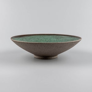 Op de afbeelding: Een brede, ondiepe keramische kom met een gespikkelde, groene glazuur aan de binnenkant en een bruine, gespikkelde glazuur aan de buitenkant.