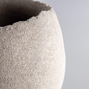 Pode incluir: Um close-up de um vaso de cer&acirc;mica cinza texturizado com uma borda &aacute;spera e irregular.