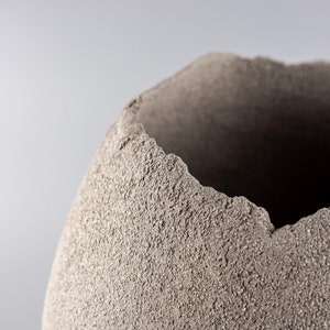 Pode incluir: Um close-up de um vaso de cer&acirc;mica cinza texturizado com uma borda &aacute;spera e irregular.