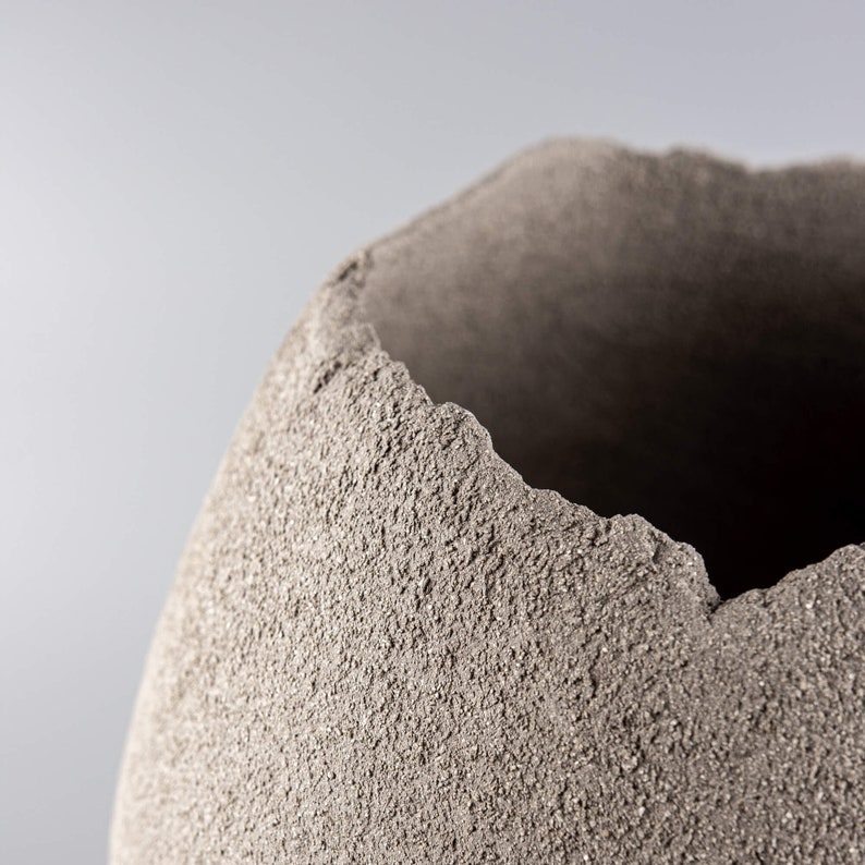 Pode incluir: Um close-up de um vaso de cer&acirc;mica cinza texturizado com uma borda &aacute;spera e irregular.