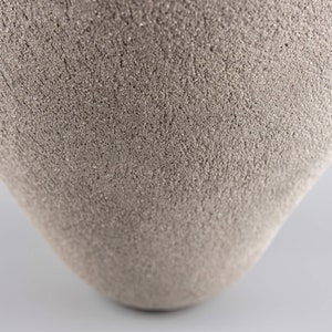 Pode incluir: Um close-up de um vaso de cer&acirc;mica cinza com uma superf&iacute;cie texturizada.
