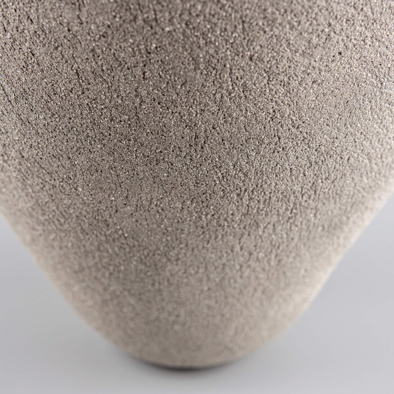 Pode incluir: Um close-up de um vaso de cer&acirc;mica cinza com uma superf&iacute;cie texturizada.