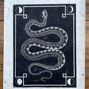 May include: A black and white print of a snake with a detailed skeletal design. The snake is coiled in a circle and is framed by a black border with white circles at each corner.