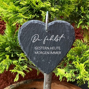 Könnte beinhalten: Ein schwarzer herzförmiger Schiefer-Gartenmarker mit dem Text "Du fehlst Gestern.Heute.Morgen.Immer" in weißer Schrift.