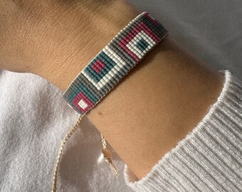 May include: A beaded bracelet with a geometric pattern in shades of gray, white, pink, and teal. The bracelet has a simple string tie closure.