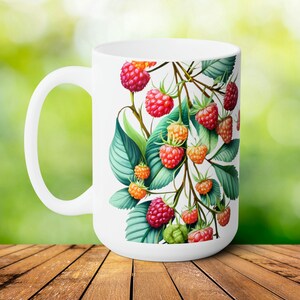 Op de afbeelding: Witte keramische mok met een ontwerp van een frambozentak met groene bladeren en rode, roze en oranje frambozen.
