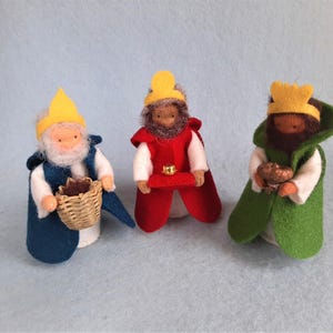May include: Three felt Wise Men figures. One wears a blue robe and holds a woven basket. Another is in a red cloak, and the third is in green. All have yellow crowns and hold gifts.