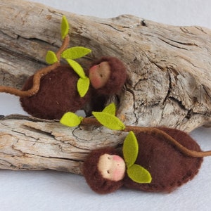 May include: Two brown felt monkey dolls with green felt leaves on a branch. The monkeys have closed eyes and rosy cheeks.