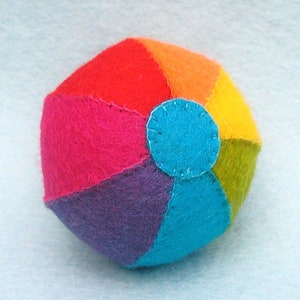 May include: A multi-colored felt beach ball with red, orange, yellow, green, blue, and purple sections. The ball is stitched together and has a blue felt circle in the center.