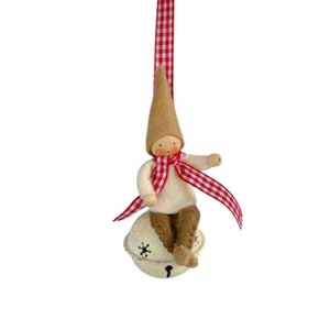 May include: A felt Christmas ornament featuring a small gnome wearing a red and white checked scarf and hat, sitting on a white bell with snowflake designs.