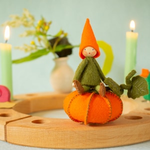 May include: A wooden advent calendar with a felt gnome sitting on a felt pumpkin. The calendar has four candles, two lit, and a felt bird.