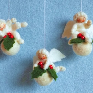 May include: Three white felt angel ornaments with red berry holly sprigs hanging from white string. Each angel is sitting on a white felt ball.