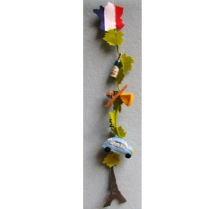 Op de afbeelding: Een vilt garland met een Frans thema. Het heeft een Franse vlag, een fles champagne, een stokbrood, een stuk kaas, een blauwe auto en de Eiffeltoren.