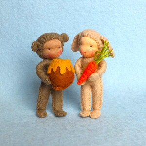 May include: Two handmade felt dolls, one dressed as a monkey holding a small yellow and orange pot, the other dressed as a bunny holding a carrot.