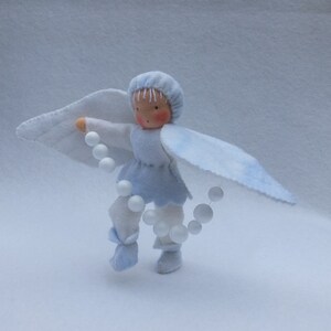 May include: A blue felt angel doll with white wings and a pearl necklace. The doll is wearing a blue dress and white boots.