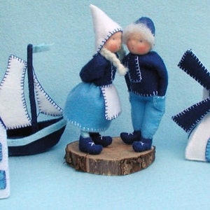 May include: A set of felt toys in blue and white, including a girl and boy doll, a windmill, a house, and a sailboat. The dolls are wearing traditional Dutch clothing.