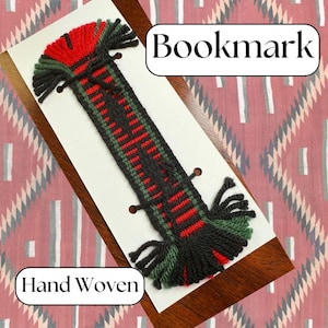 May include: Hand-woven bookmark with a rectangular design. The bookmark features a black, red, and green pattern with fringe at both ends. The word "Bookmark" is displayed at the top, and "Hand Woven" is at the bottom.