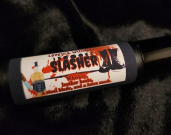 Może przedstawiać: Niebieska i czarna butelka z czerwoną i białą etykietą, na której widnieje napis "Lovesick Witchery Slasher". Etykieta zawiera również rysunek butelki whisky, skórzanych butów, stalowego ostrza i lateksowej maski. Tekst na etykiecie brzmi: "Whisky, skórzane buty, stalowe ostrze i lateksowa maska."