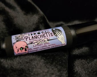 May include: A black and purple tube with a label that says "Lovesick Witchery Planchette" and lists the ingredients: lavender, herbs, milk, sugar, vanilla, incense, labdanum, heliotrope, cashmeran, and black musk.