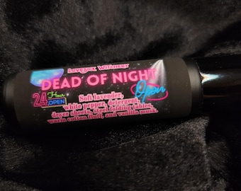 Peut inclure: Un produit cylindrique noir avec le texte "DEAD OF NIGHT" en rose et blanc, et "24 Hour Open" en bleu. L'étiquette énumère des ingrédients comme la lavande douce, le poivre blanc et la vanille musquée. Le produit est posé sur un fond sombre et texturé.
