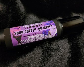 May include: A black roller bottle with a purple label that reads "LOVESICK WITCHERY YOUR COFFIN, OR MINE?" with a description of the scent: "Blackened rose, dark honey, cardamom creme, amber, and velveteen black cashmere."