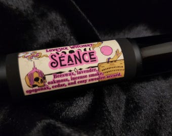 May include: A black and white label with pink accents reads "LOVESICK WITCHERY SÉANCE" and lists the scent notes: beeswax, lavender, oakmoss, incense smoke, opoponax, cedar, and cozy sweater accord.