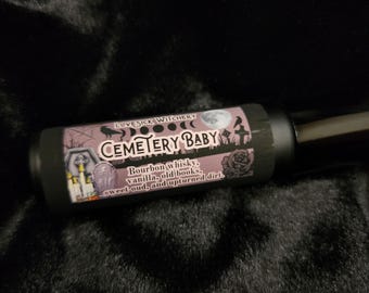 May include: A black roll-on bottle with a label that reads "LOVESICK WITCHERY CEMETERY BABY Bourbon whisky, vanilla, old books, sweet oud, and upturned dirt."