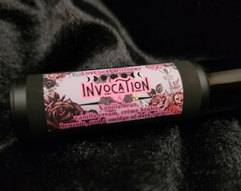 May include: A black roller bottle with a pink and white label that says "LOVESICK WITCHERY INVOCATION Vanilla bean, vanilla cream, crème brûlée benzoin, and a smidge of dark amber".