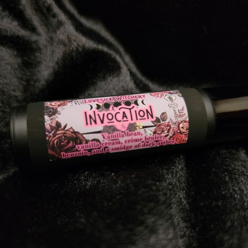 May include: A black roller bottle with a pink and white label that says "LOVESICK WITCHERY INVOCATION Vanilla bean, vanilla cream, creme brulee benzoin, and a smidge of dark amber".