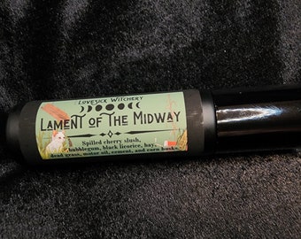 May include: A black roller bottle with a white label that reads "LOVESICK WITCHERY LAMENT OF THE MIDWAY" with a moon and star design. The label also includes a description of the scent: "Spilled cherry slush, bubblegum, black licorice, hay, dead grass, motor oil, cement, and corn husks."
