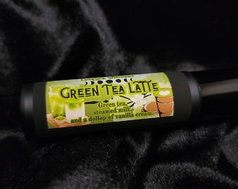 May include: A black roll-on bottle with a green, white, and brown label that reads "GREEN TEA LATTE" and describes the drink as "Green tea, steamed milk, and a dollop of vanilla cream."