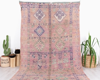 May include: A pink and purple Moroccan rug with a geometric pattern. The rug has a fringe border and is made of wool.
