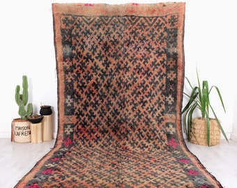 Puede incluir: Una alfombra marroquí vintage con un patrón geométrico en tonos marrones, negros y rojos. La alfombra tiene un aspecto desgastado y está tejida con un hilo grueso y texturizado.