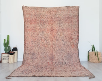 May include: A large, rectangular, vintage rug with a faded, abstract pattern in shades of pink, brown, and gray. The rug is laid out on a light wood floor.