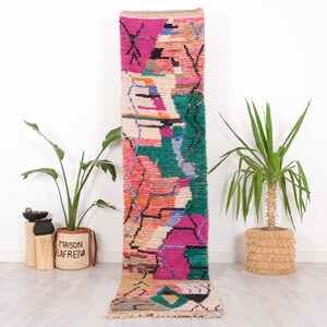 May include: A colorful, rectangular runner rug with a geometric design. The rug features a vibrant mix of pink, green, orange, and blue hues. The rug is made of a soft, textured material and is suitable for hallways or entryways.