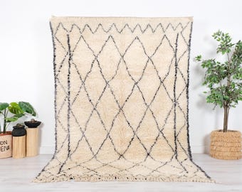 May include: A white and black Moroccan rug with a diamond pattern. The rug has a fringe border and is made of wool.