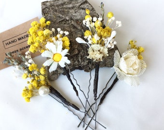 May include: Five hair pins with yellow and white dried flowers, a white pearl bead, and a piece of wood with the text "HAND MADE" and "beze acces".