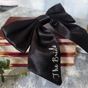 Könnte beinhalten: Eine schwarze Schleife aus Satin mit den Worten "The Bride" in weiß gestickt.