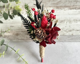 Boutonnière da sposa invernale con pigna, fiori rossi e bordeaux, boutonnière rustica per lo sposo a tema bosco.