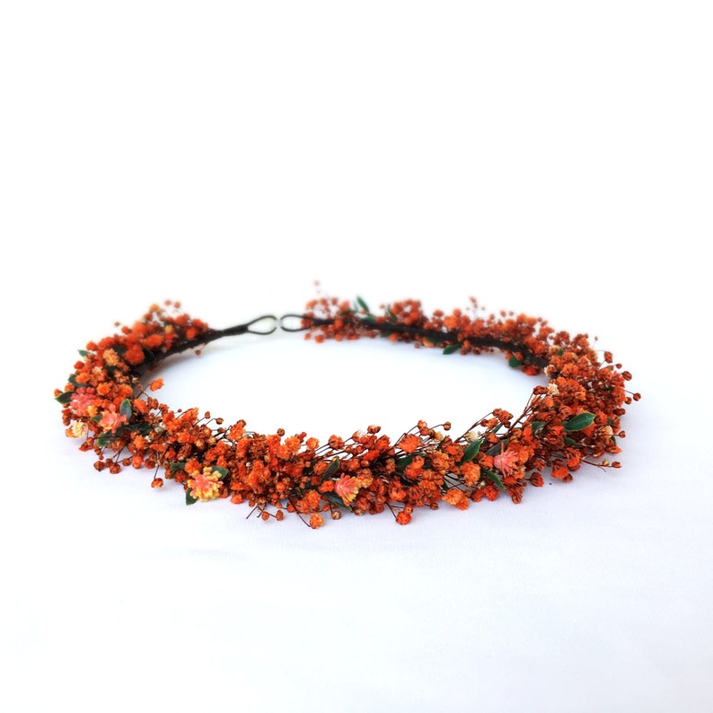 May include: A floral crown made of dried orange flowers and greenery. The crown is made on a wire base and is perfect for a wedding or other special occasion.
