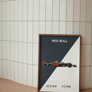 Puede incluir: Un póster enmarcado con un diseño en blanco y negro. El póster presenta un coche de carreras de Fórmula 1 rojo y amarillo con el texto "Red Bull" en el lateral. El póster también incluye el texto "33 | VER 11 | PER".
