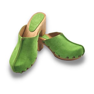 May include: A pair of green suede clogs with wooden heels. The clogs have a rounded toe and a small heel.