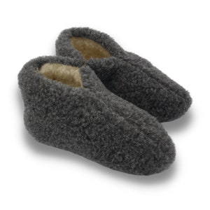 Op de afbeelding: Een paar grijze wollen pantoffels met een pluche textuur. De pantoffels hebben een bruine fleece voering.