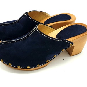 May include: A pair of navy blue suede clogs with wooden heels and gold studs around the edges.