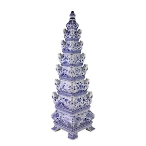 May include: A tall, white ceramic flower vase with a blue and white floral design. The vase is shaped like a pyramid with a square base and multiple tiers. It has a traditional Dutch Delftware style.