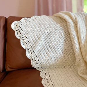 May include: A white crocheted throw blanket with a scalloped edge, draped over a brown leather sofa.