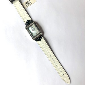 Puede incluir: Un reloj blanco con una esfera rectangular y una correa blanca. La esfera del reloj tiene n&uacute;meros romanos y est&aacute; rodeada de peque&ntilde;os cristales. La correa tiene un patr&oacute;n de cocodrilo. El reloj tiene una etiqueta que dice "Jolie Montre Chameleon".